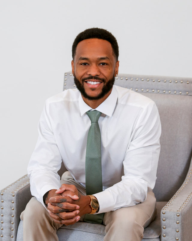 Professional-headshot-brand-stylish black man in white shirt with green tie in a nailhead trimmed grey luxury chair East Peoria headshots with style